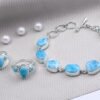 Close-up of elegant silver jewelry with larimar stones and pearls on textured fabric.